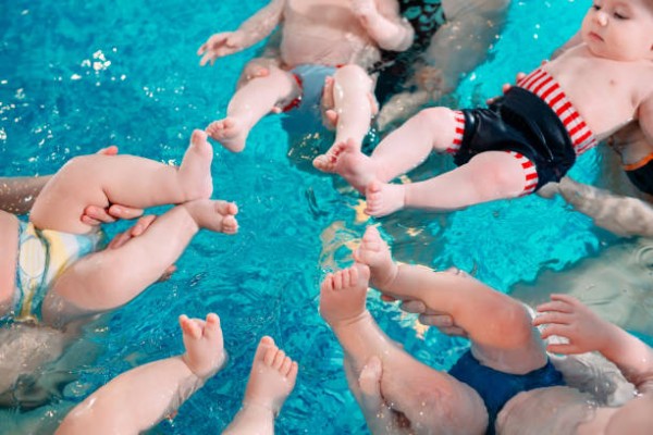 Babies in a parent and tot swim class floating in a pool with adults supporting them.